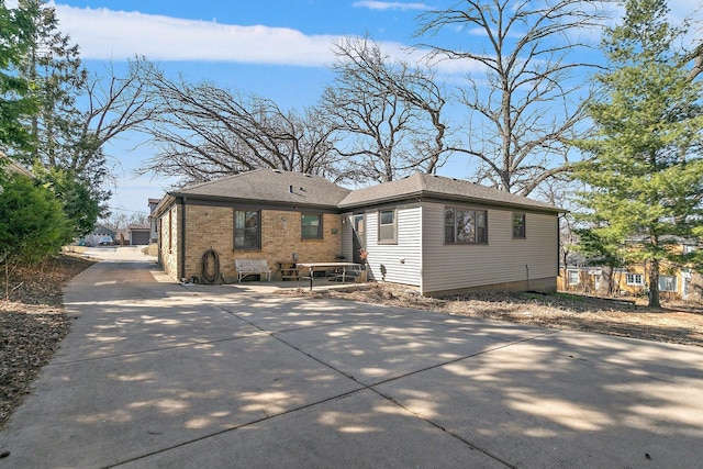 back of house featuring brick siding, roof with shingles, and concrete driveway