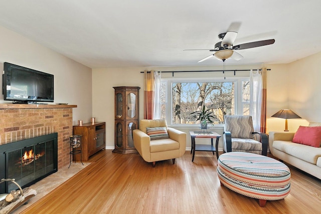 living area featuring a ceiling fan, a brick fireplace, wood finished floors, and baseboards