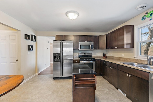 kitchen with a sink, a kitchen island, dark brown cabinetry, appliances with stainless steel finishes, and baseboards