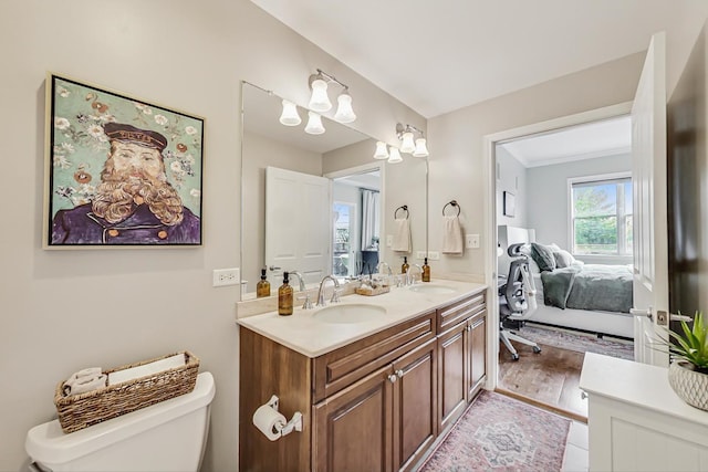 ensuite bathroom featuring double vanity, toilet, a sink, and wood finished floors