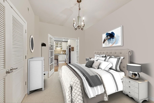 bedroom featuring an inviting chandelier, light colored carpet, a closet, and freestanding refrigerator