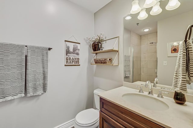 bathroom with baseboards, vanity, toilet, and tiled shower