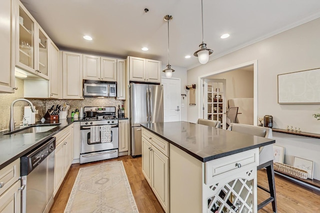 kitchen featuring stainless steel appliances, a sink, light wood-style floors, a kitchen breakfast bar, and dark countertops