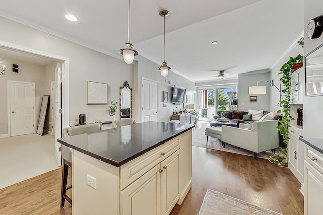 kitchen featuring cream cabinetry, a kitchen bar, dark countertops, dark wood finished floors, and crown molding