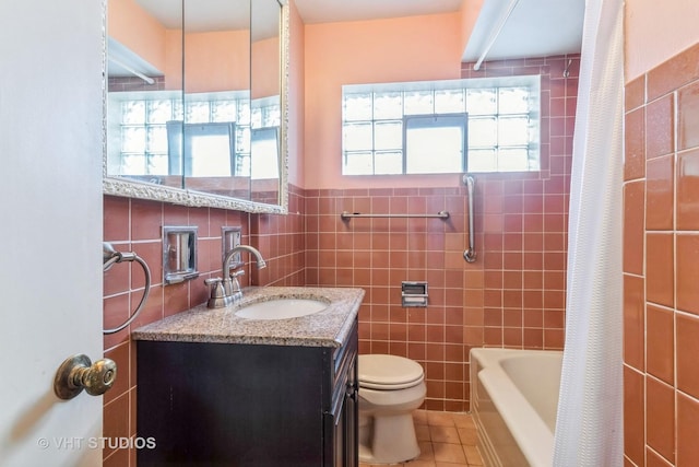 full bathroom with toilet, plenty of natural light, vanity, and tile walls