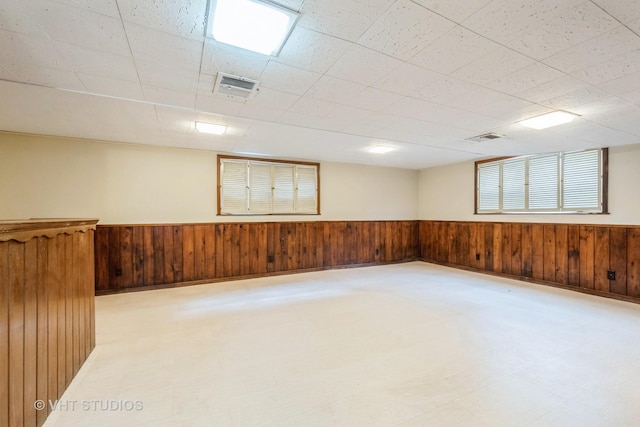 below grade area featuring a wainscoted wall, wooden walls, visible vents, and light floors