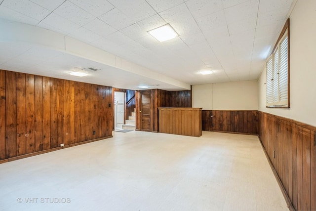 below grade area with light floors, visible vents, wainscoting, wooden walls, and stairs