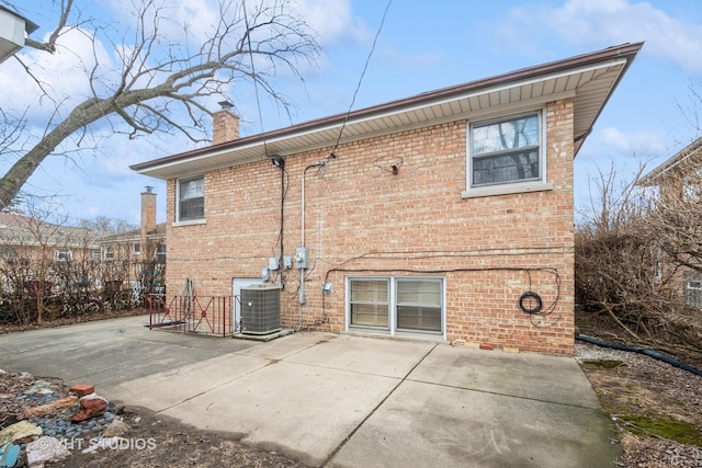 back of property with a patio, brick siding, a chimney, and central AC unit