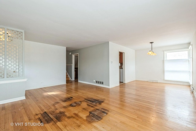 empty room with light wood-style floors, baseboards, stairs, and visible vents