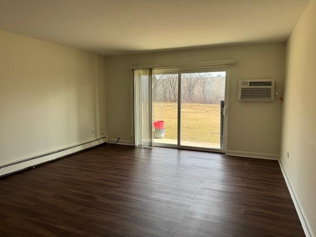 empty room with baseboards, baseboard heating, dark wood-type flooring, and a wall mounted AC