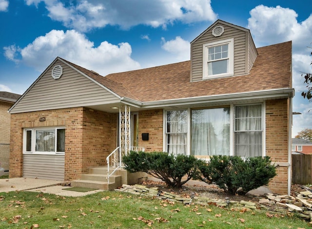 view of front of house featuring a shingled roof, a front lawn, and brick siding