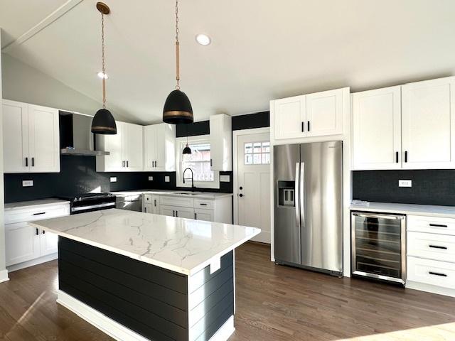 kitchen with a sink, wall chimney range hood, gas range, beverage cooler, and stainless steel fridge