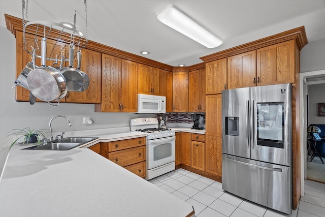 kitchen featuring light tile patterned floors, light countertops, brown cabinetry, a sink, and white appliances