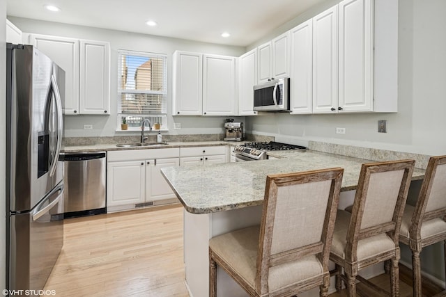 kitchen featuring stainless steel appliances, a peninsula, a sink, white cabinets, and a kitchen bar