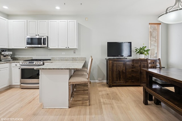 kitchen with light wood finished floors, a breakfast bar area, stainless steel appliances, white cabinetry, and light stone countertops