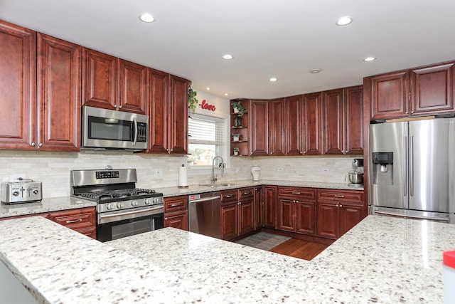 kitchen with open shelves, light stone countertops, stainless steel appliances, and a sink