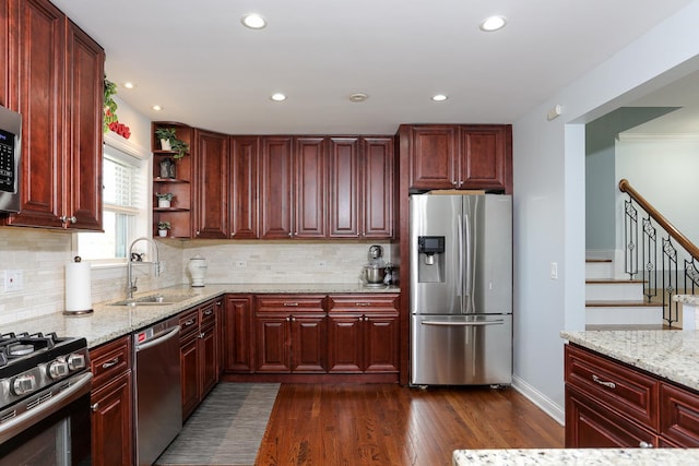 kitchen with dark wood-style floors, appliances with stainless steel finishes, light stone counters, and a sink