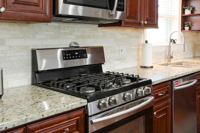 kitchen with reddish brown cabinets, light stone counters, backsplash, appliances with stainless steel finishes, and a sink