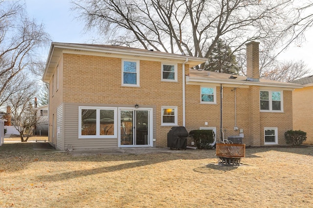 rear view of house with cooling unit, brick siding, a lawn, and a chimney