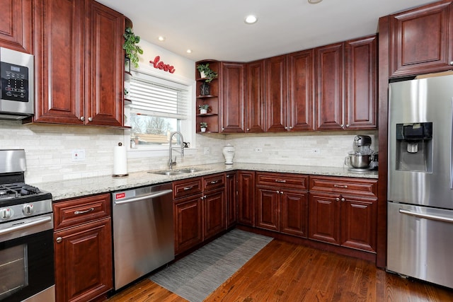 kitchen featuring stainless steel appliances, dark wood finished floors, a sink, and light stone counters