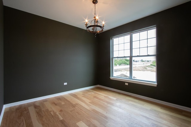 spare room featuring a chandelier, light wood-type flooring, and baseboards