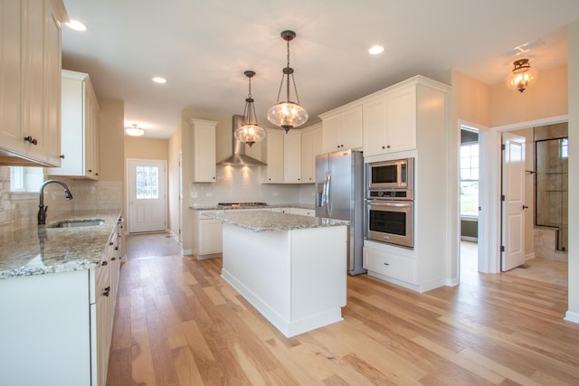 kitchen with light wood finished floors, appliances with stainless steel finishes, a center island, white cabinetry, and a sink