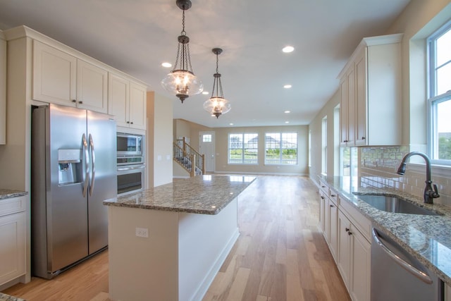 kitchen featuring backsplash, light wood-style flooring, stainless steel appliances, and a sink