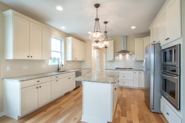 kitchen with wall chimney exhaust hood, a kitchen island, stainless steel appliances, light wood-type flooring, and a sink