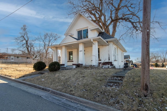 view of front facade featuring a porch, roof with shingles, fence, and stucco siding