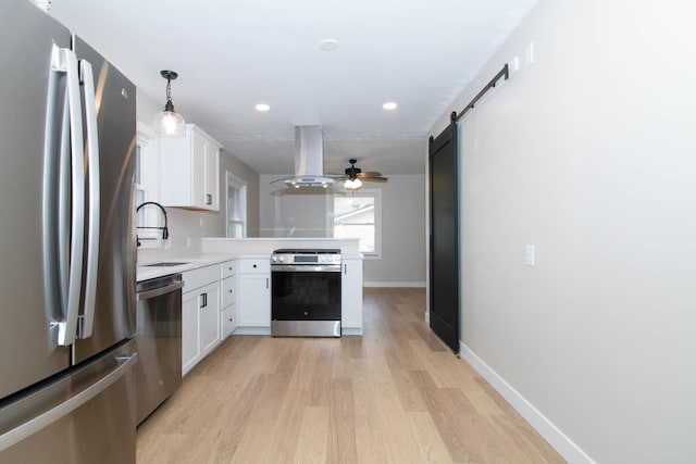 kitchen featuring a barn door, a peninsula, island exhaust hood, stainless steel appliances, and a sink