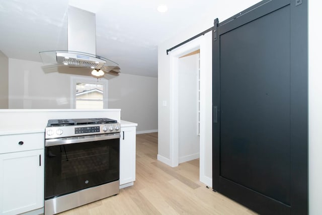 kitchen featuring a barn door, light wood-style flooring, island exhaust hood, light countertops, and gas stove