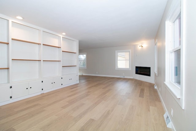 unfurnished living room with recessed lighting, visible vents, baseboards, light wood-type flooring, and a glass covered fireplace