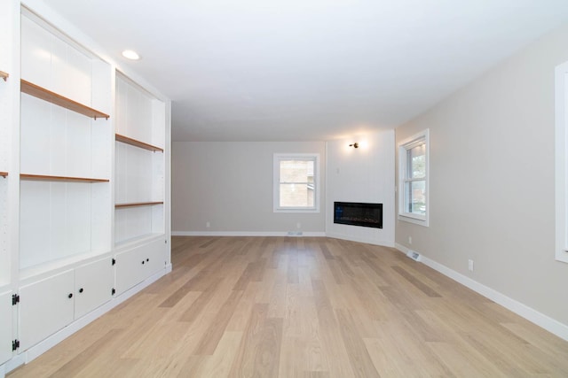 unfurnished living room with recessed lighting, visible vents, baseboards, light wood-style floors, and a glass covered fireplace