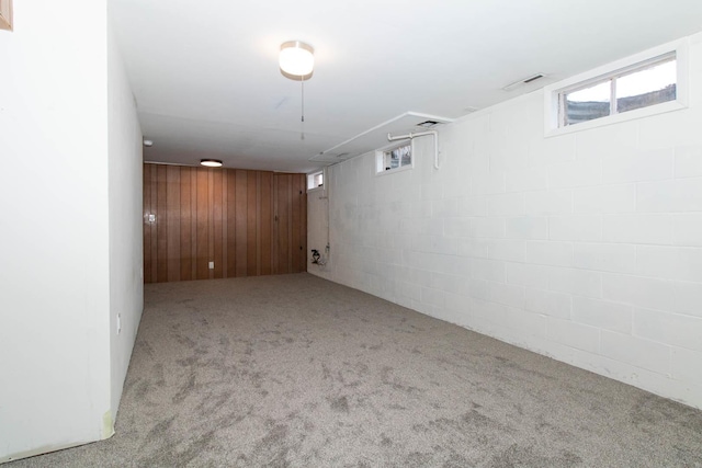 basement featuring a wealth of natural light, wood walls, carpet flooring, and visible vents