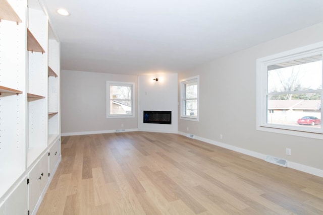 unfurnished living room featuring light wood-type flooring, baseboards, visible vents, and a glass covered fireplace