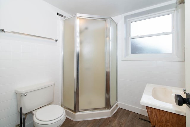 bathroom featuring toilet, wood finished floors, vanity, tile walls, and a stall shower