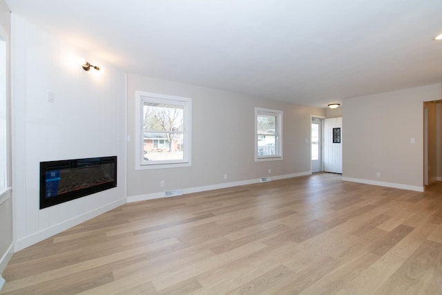 unfurnished living room with a healthy amount of sunlight, a large fireplace, light wood-type flooring, and baseboards