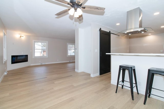 kitchen with a barn door, light wood-type flooring, island exhaust hood, and a glass covered fireplace