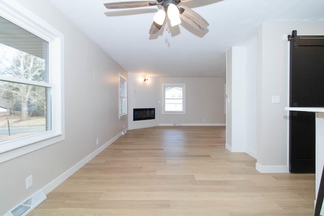 unfurnished living room featuring baseboards, visible vents, a ceiling fan, a glass covered fireplace, and light wood-type flooring