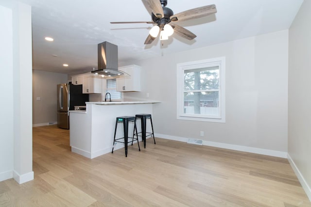 kitchen with island exhaust hood, freestanding refrigerator, white cabinets, a peninsula, and a kitchen breakfast bar