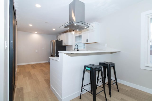 kitchen with a breakfast bar, white cabinets, light countertops, freestanding refrigerator, and island exhaust hood