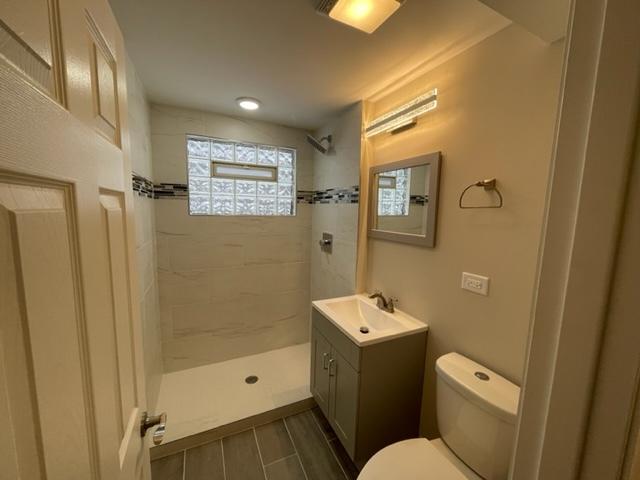 full bath with tiled shower, wood finish floors, vanity, and toilet