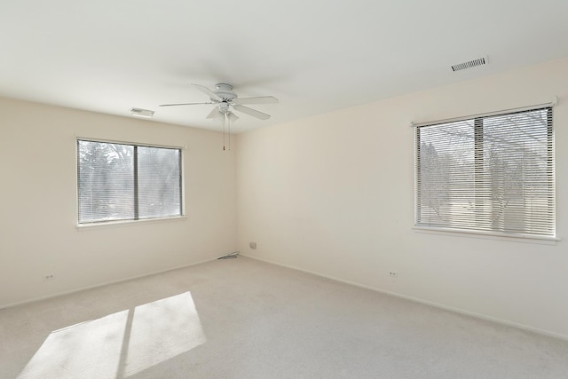 unfurnished room with a ceiling fan, light colored carpet, visible vents, and baseboards