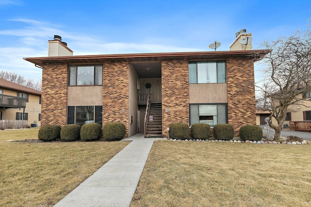 view of front of property with stairway, a front yard, brick siding, and a chimney