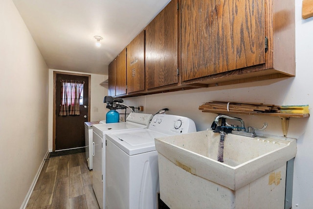 clothes washing area with wood finished floors, a sink, baseboards, washer and dryer, and cabinet space