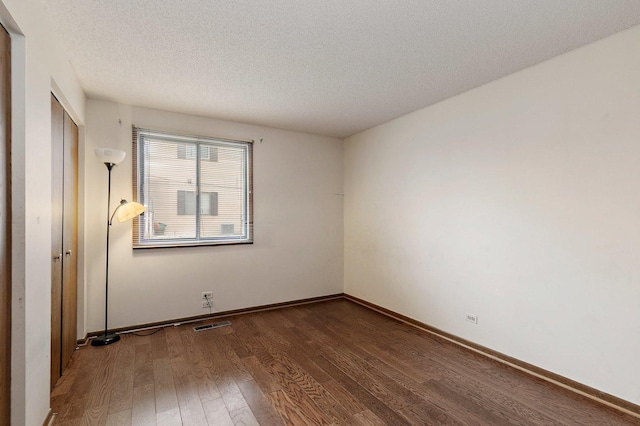 empty room featuring dark wood-type flooring, visible vents, a textured ceiling, and baseboards