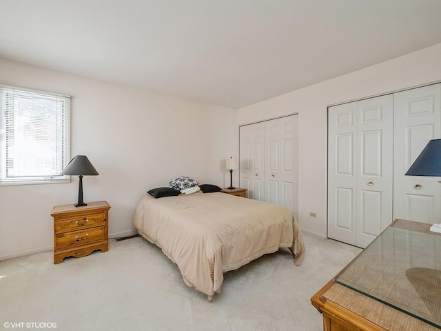 bedroom with multiple closets, light colored carpet, and baseboards