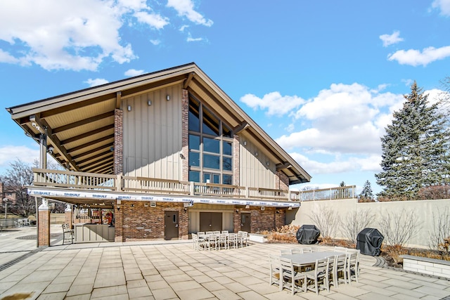 back of property with board and batten siding, brick siding, and a patio