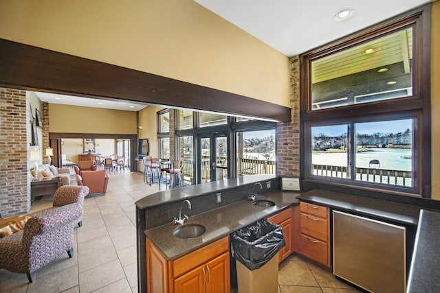 bar featuring a water view, light tile patterned floors, brick wall, and a sink