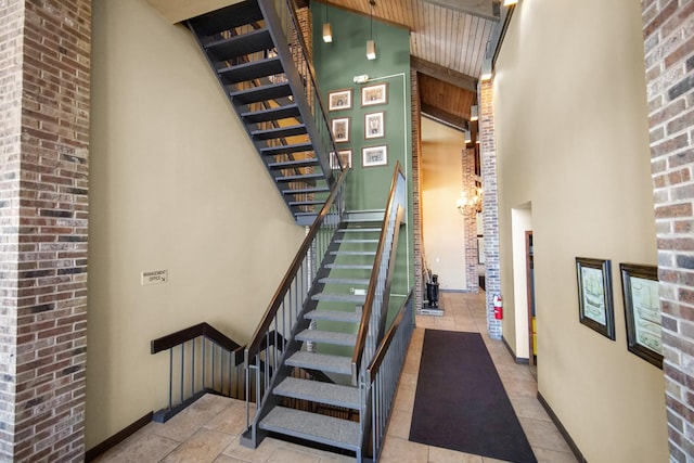 stairway featuring baseboards, a towering ceiling, brick wall, and tile patterned floors